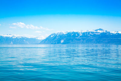 Scenic view of snowcapped mountains by sea against blue sky