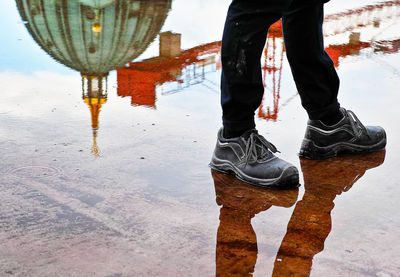 Low section of man walking by berlin cathedral reflection on walkway in rainy season