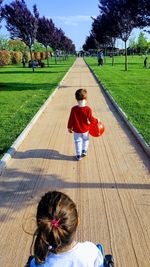 Siblings on footpath against trees in sunny day