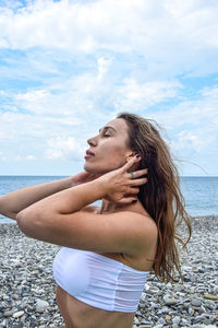 Young woman standing at beach against sky