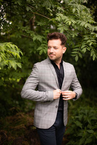 Handsome man wearing suit looking away while standing against plants