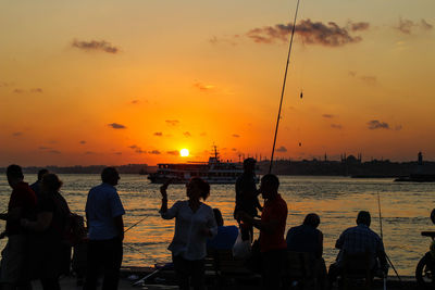 Silhouette people on beach against orange sky