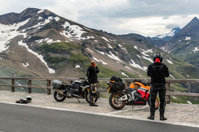 People riding bicycles on road by mountain against sky