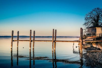 Wooden posts in sea against clear blue sky