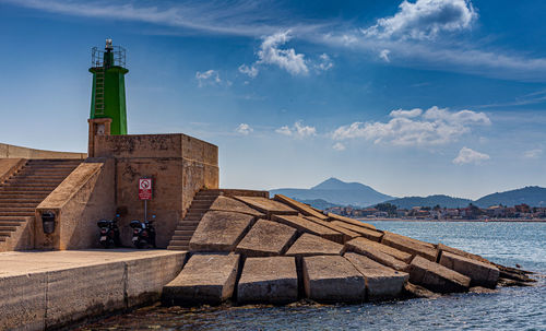 Lighthouse amidst buildings and sea against sky