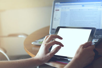 Mockup image of hands holding black tablet pc with blank white desktop screen while sitting in cafe