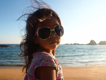 Portrait of girl wearing sunglasses standing at beach against clear sky