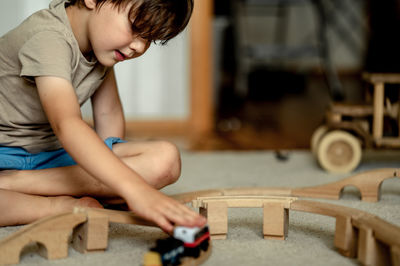 The boy is playing by train at home. the child is building a railway from a wooden construction set