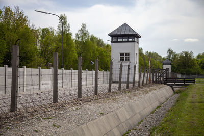 Fence by trees and building against sky in dachau 