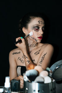 Woman with text on body applying make-up against black background