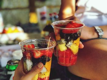 Close-up of friends holding fruits in disposable glasses