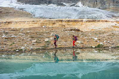 Glacier reflects in alpine lake while walking alongside lake's shores