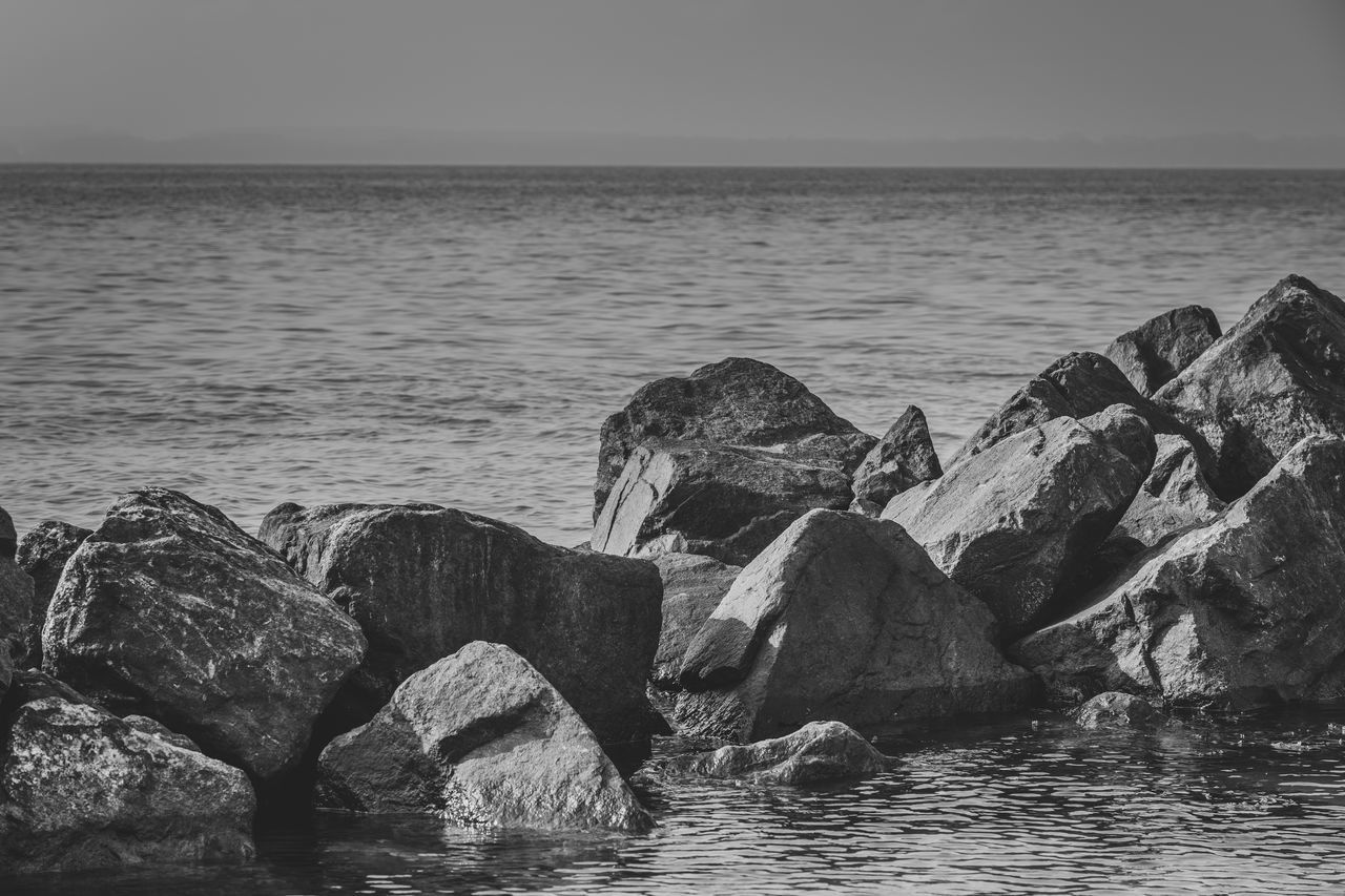 water, sea, rock, horizon over water, sky, black and white, horizon, scenics - nature, beauty in nature, nature, land, beach, coast, ocean, wave, shore, monochrome photography, monochrome, tranquility, tranquil scene, no people, rock formation, outdoors, day, non-urban scene, idyllic, clear sky, bay, seascape