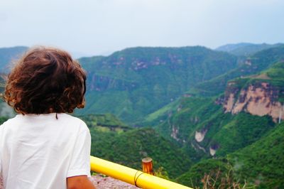 Rear view of boy looking at mountain against clear sky