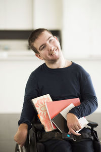 Disabled man with books sitting on wheelchair at home