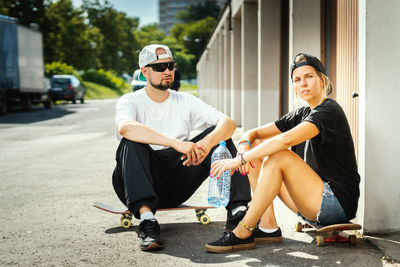 Portrait of couple with skateboards sitting in city