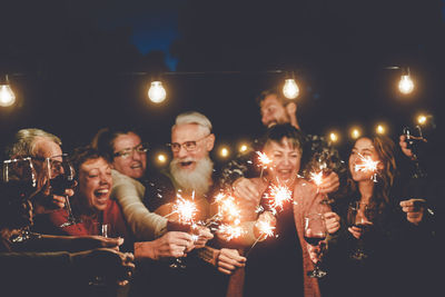 Happy friends holding illuminated sparklers at night