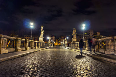 Cobbled road at illuminated bridge against sky