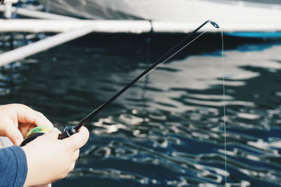 Cropped hand of child holding fishing rod in lake