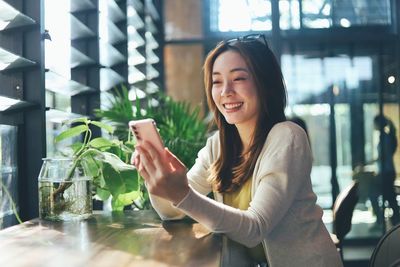 Young woman using mobile phone while sitting on table