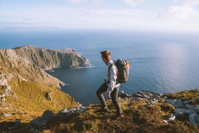 Man standing on rock by sea against sky