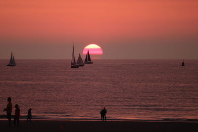 Silhouette people on sea against orange sky