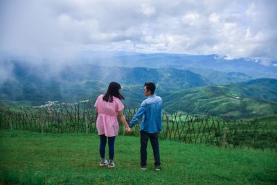 Rear view of couple holding hands while standing on mountain against sky