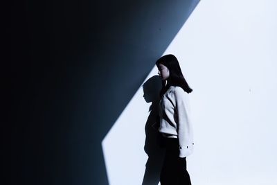 Side view of young woman standing against wall