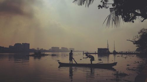 People on boat in river against sky during sunset