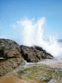 Sea waves splashing on rocks against sky