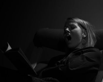 Woman with book yawning while relaxing on chair