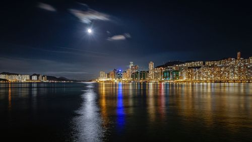 Victoria harbour by illuminated city against sky at night