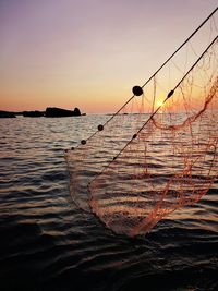 Silhouette fishing net on sea against sky during sunset