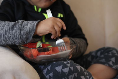 Midsection of boy eating fruits while sitting on sofa at home