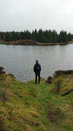 Rear view of man looking at lake against sky