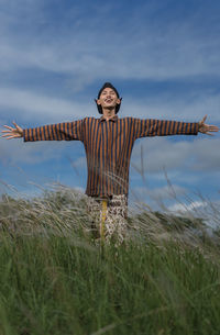Smiling man with arms outstretched standing on field against sky