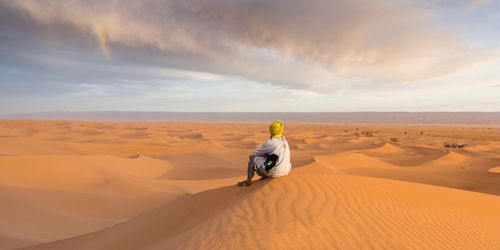 Man sitting at desert against sky