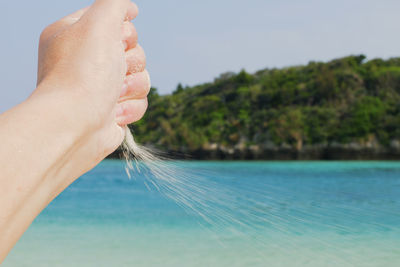 Cropped image of kid blowing sand against sea