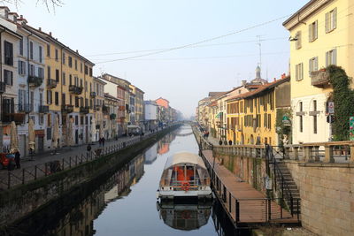 Boats in canal amidst city against clear sky