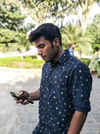 Young man using phone while standing at park