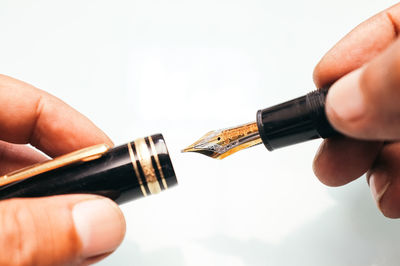 Close-up of hands holding fountain pen against white background