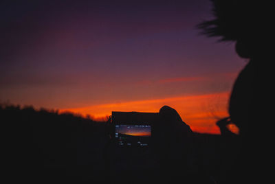 Silhouette person photographing orange sky during sunset