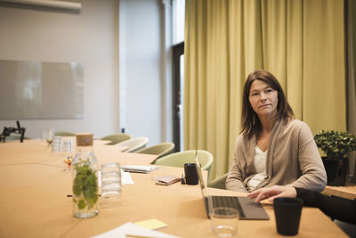 Serious businesswoman sitting with colleague at conference table in board room