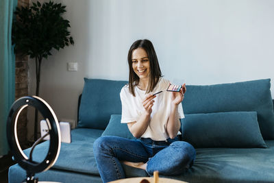 Smiling female influencer showing make-up palette during tutorial vlog