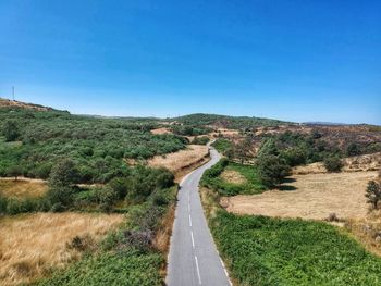 Road leading towards landscape against clear blue sky