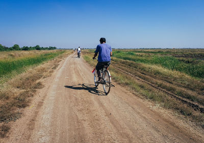 Rear view of man riding bicycle on dirt road