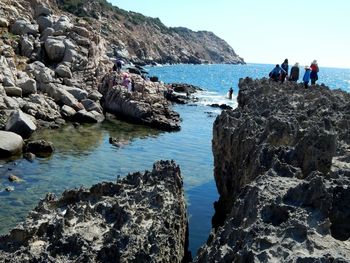 People standing on cliff by sea against clear sky