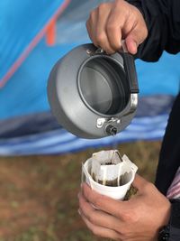 Cropped hand of person pouring hot water in tea cup at campsite