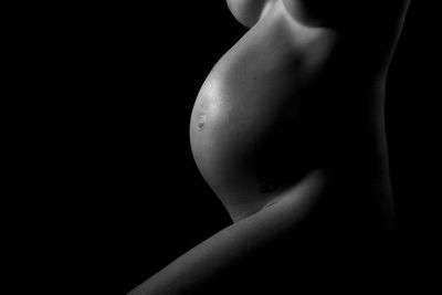 Midsection of naked pregnant woman standing on black background