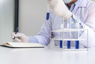 Midsection of scientist with book and liquid on desk at laboratory